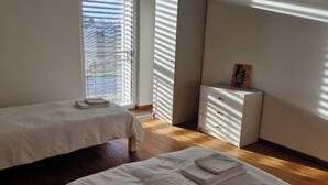 Une chambre avec deux lits, une commode et une fenêtre avec des stores.