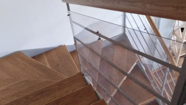 Un escalier en bois avec une rampe métallique et une balustrade en verre.