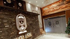 Un espace d’accueil avec un mur en pierre sombre, un grand logo illuminé et une vue sur l’entrée d’une pièce dotée d’une porte en verre.