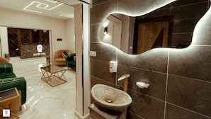 Une salle de bain moderne avec un lavabo en pierre, un miroir et un canapé vert dans l’espace de vie adjacent.