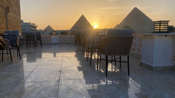 Une terrasse sur le toit offrant une vue sur les pyramides au coucher du soleil, avec des sièges modernes et un espace bar.