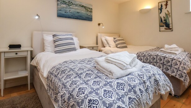 A hotel room with two beds, a painting of a coastal scene, and a wall-mounted artwork. - Powder Keg (Whitby)