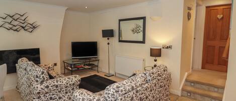 A living room with two patterned sofas, a flat-screen TV, a coffee table, and a framed picture on the wall.