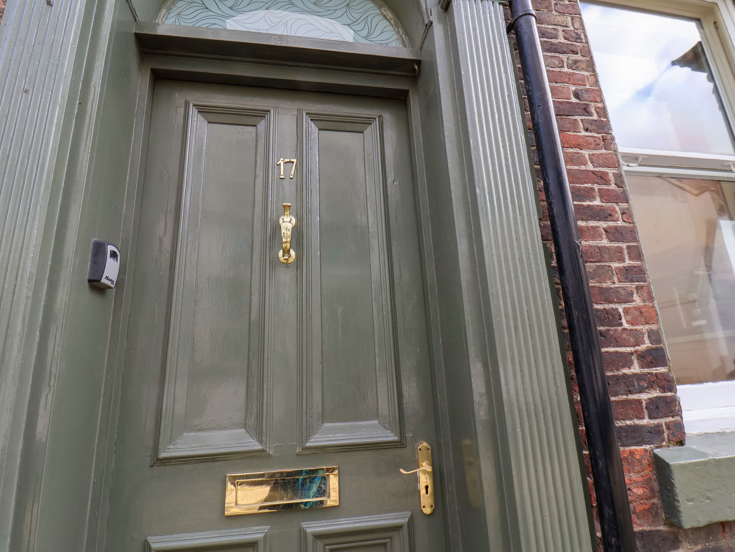 A green door with a brass knocker, a mailbox, and a window with a decorative glass design.