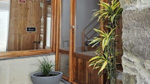 A modern building with large wooden-framed glass doors, a stone wall, and potted plants. - Casa do Cinzeiro, Açores - With private pool! (Açores)