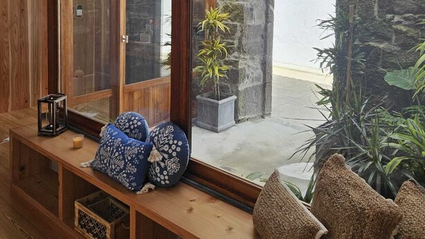 A wooden bench with cushions, a lantern, and a view of a stone building through a large window. - Casa do Cinzeiro, Açores - With private pool! (Açores)
