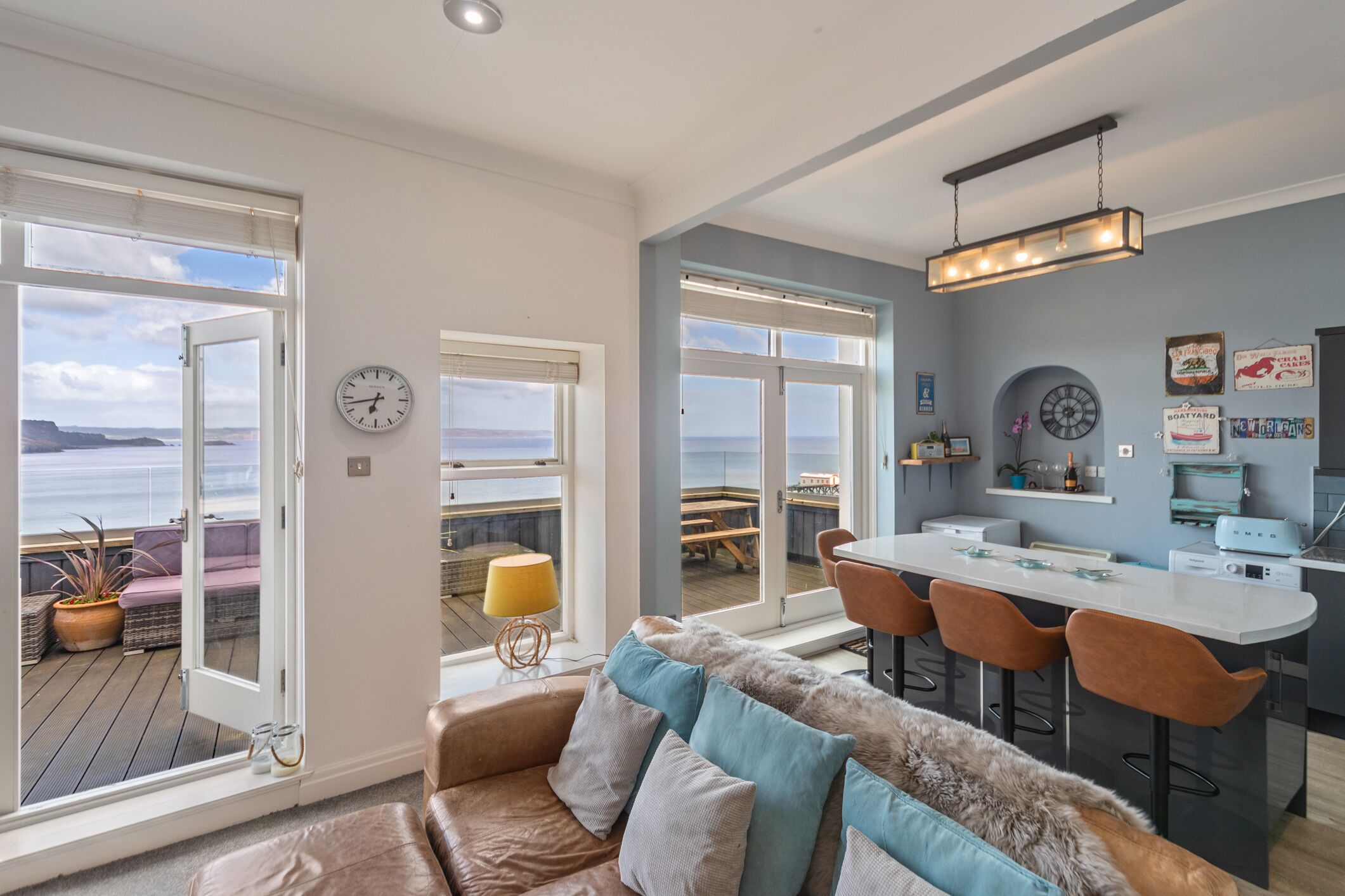 A modern kitchen with a bar area, large windows with ocean views, and a cozy seating area with a sofa and cushions.
