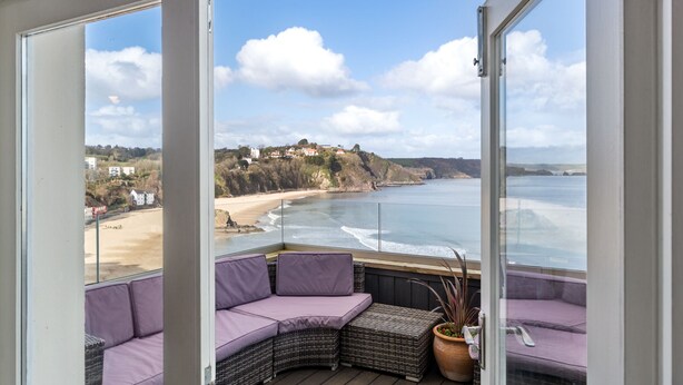 A balcony with wicker furniture and a view of the beach and ocean.