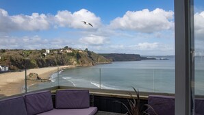 A balcony with wicker furniture and a view of the beach and sea.