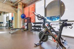 A gym with exercise equipment, including a Peloton bike, dumbbells, and a bench.