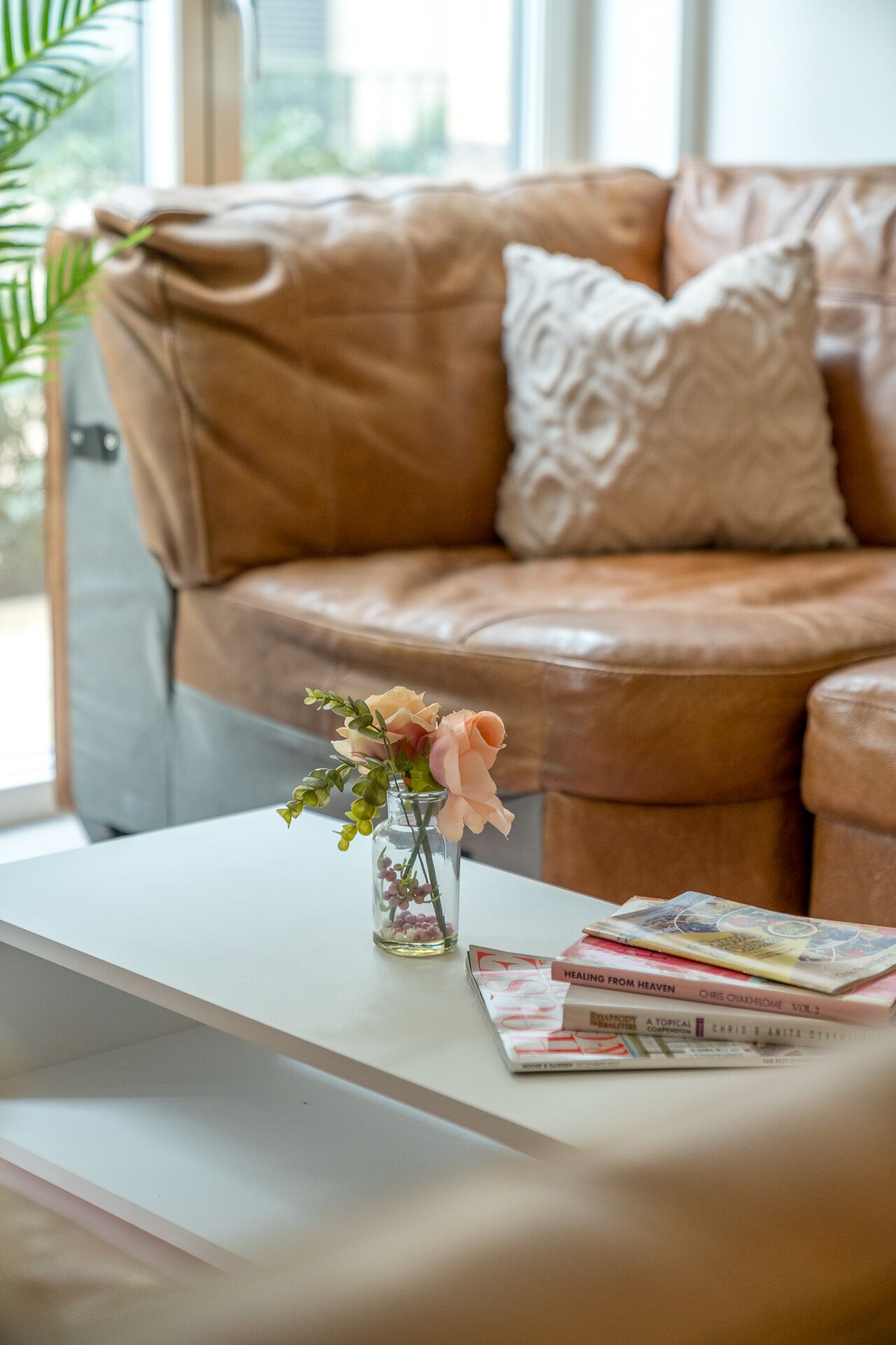 A living room with a brown leather sofa, a white coffee table, and a vase with flowers.