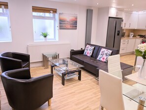 A modern living room with a glass coffee table, leather sofa, and a dining area with a glass table.