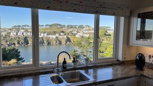 A kitchen with a large window overlooking a scenic view of a lake and houses. - Trebarfoote - Three Bedroom Cottage, Sleeps 6 (Polruan)