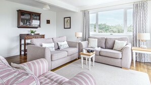 A modern living room with two sofas, a coffee table, and a side table. There is a window with curtains, a lamp, and a framed picture on the wall. - Trebarfoote - Three Bedroom Cottage, Sleeps 6 (Polruan)