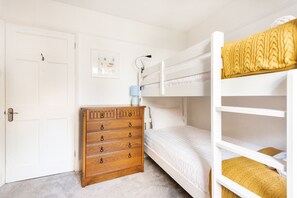 Ein Schlafzimmer mit Etagenbett, einer Holzkommode mit Schubladen, einem gerahmten Bild an der Wand und einer Tür.