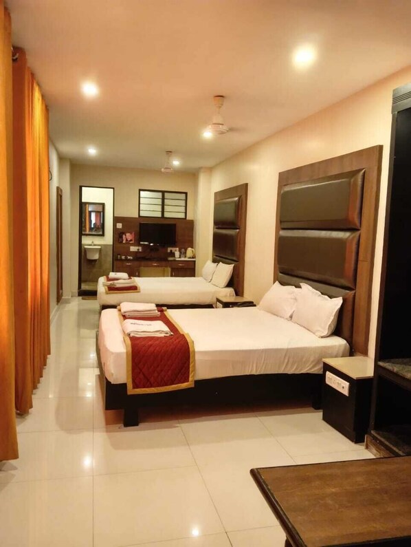 Quarto de hotel com duas camas, uma escrivaninha e um banheiro visível ao fundo.
