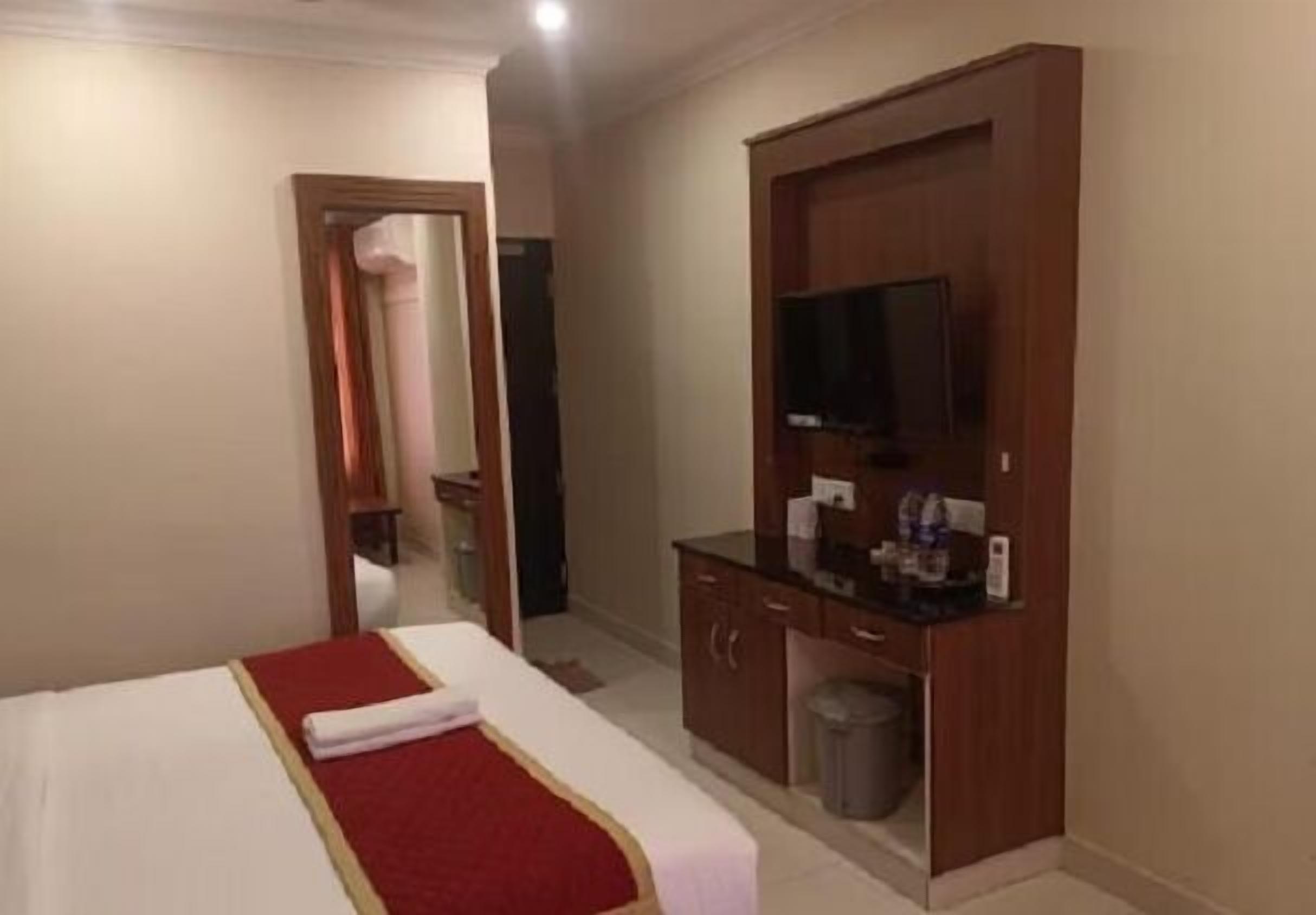 Een hotelkamer met een bed, een televisie, een bureau met een computer en een prullenbak.