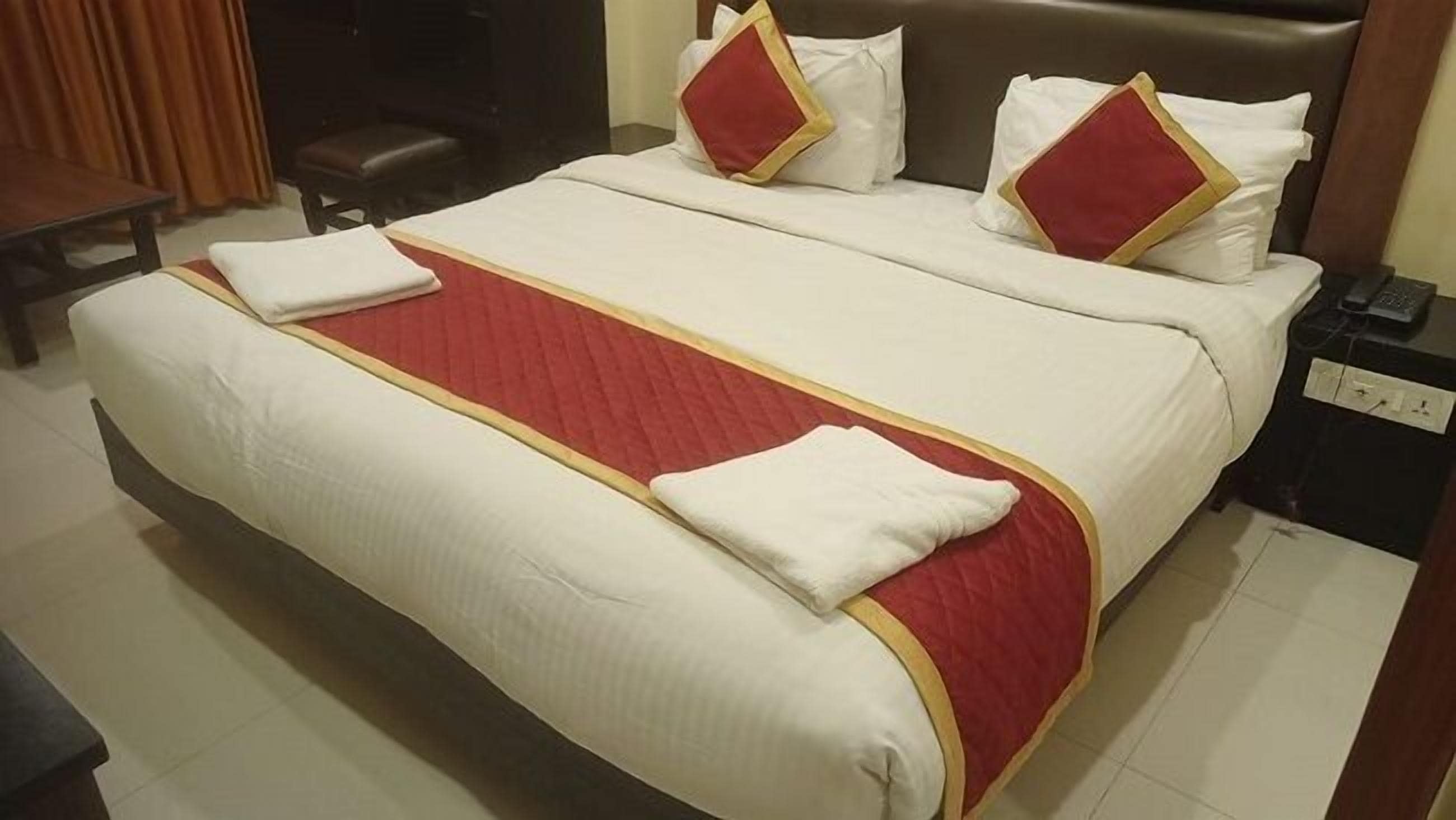 Une chambre d’hôtel avec un grand lit, deux oreillers, une couvre-lit rouge et blanche et une petite table de chevet avec un téléphone.