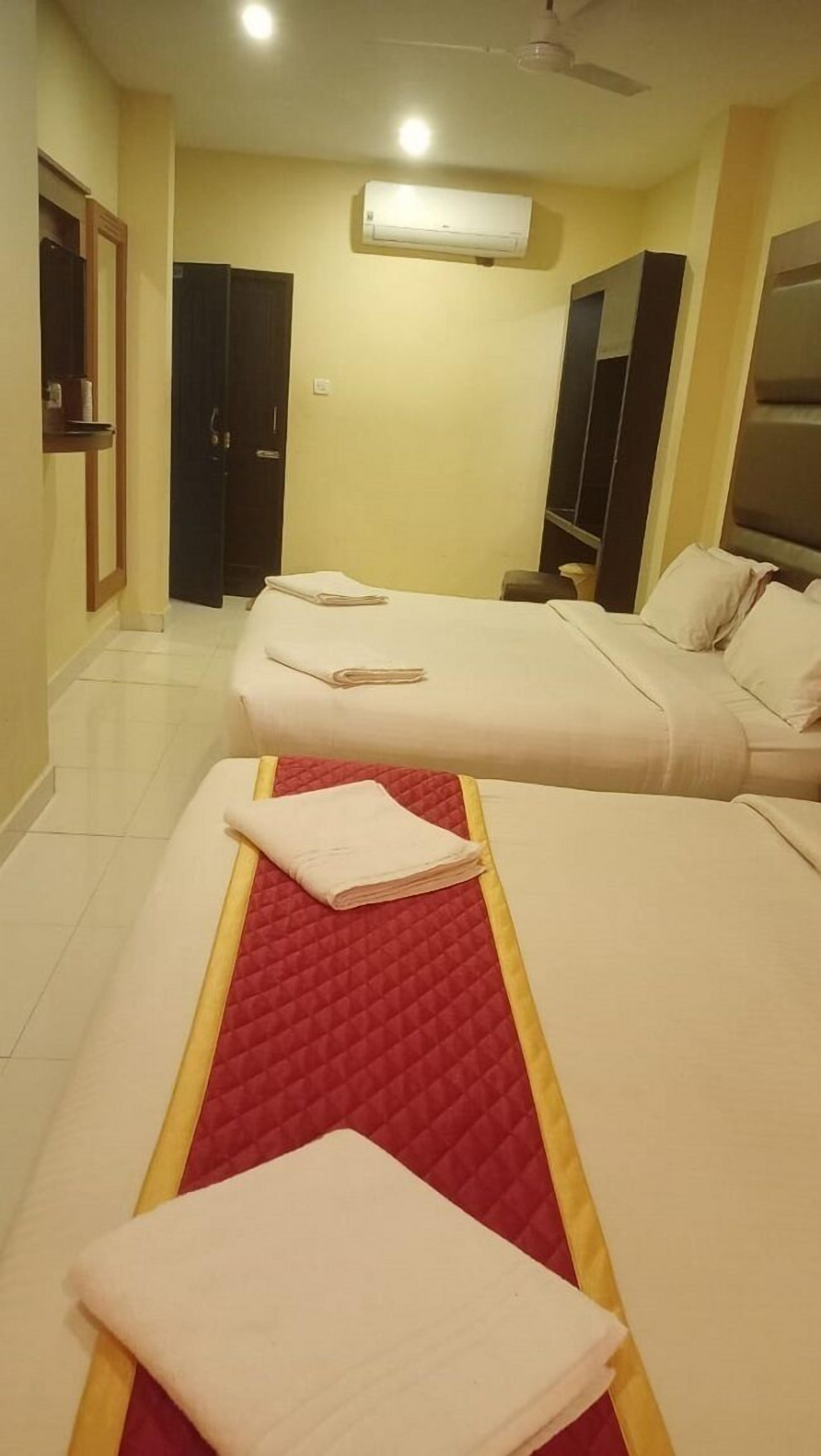 A hotel room with two beds, a red quilted bedspread, and a white bedspread.