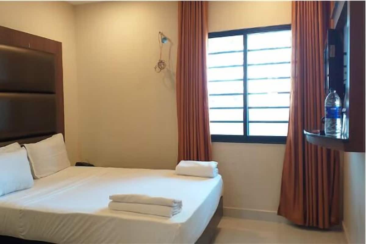 Ein Hotelzimmer mit einem großen Bett, einem Kopfteil, einem Fenster mit Vorhängen und einem an der Wand befestigten Regal mit einer Flasche.