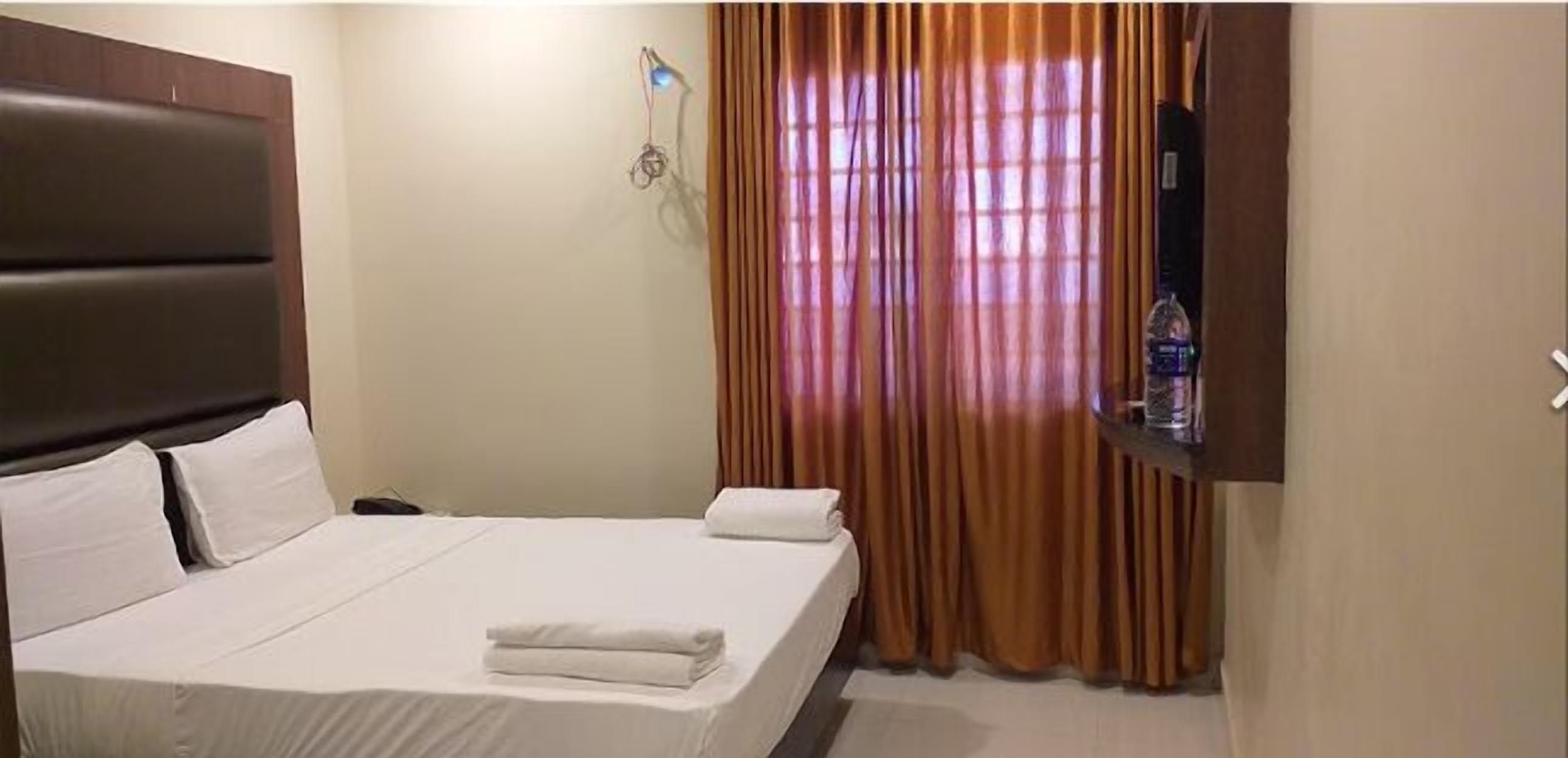 Una camera d'albergo con un letto, un comodino, una televisione e una finestra con tende.