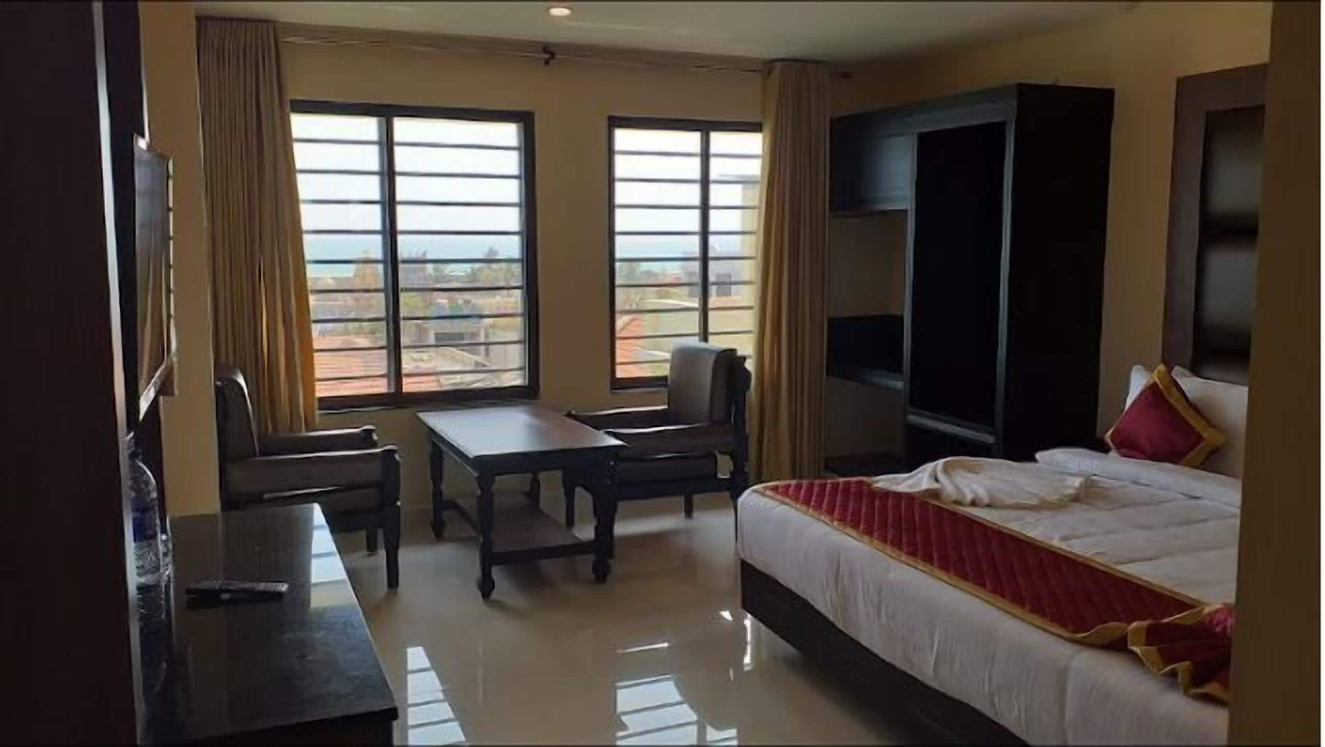 A hotel room with a bed, a desk, two chairs, a TV, and large windows with a view.