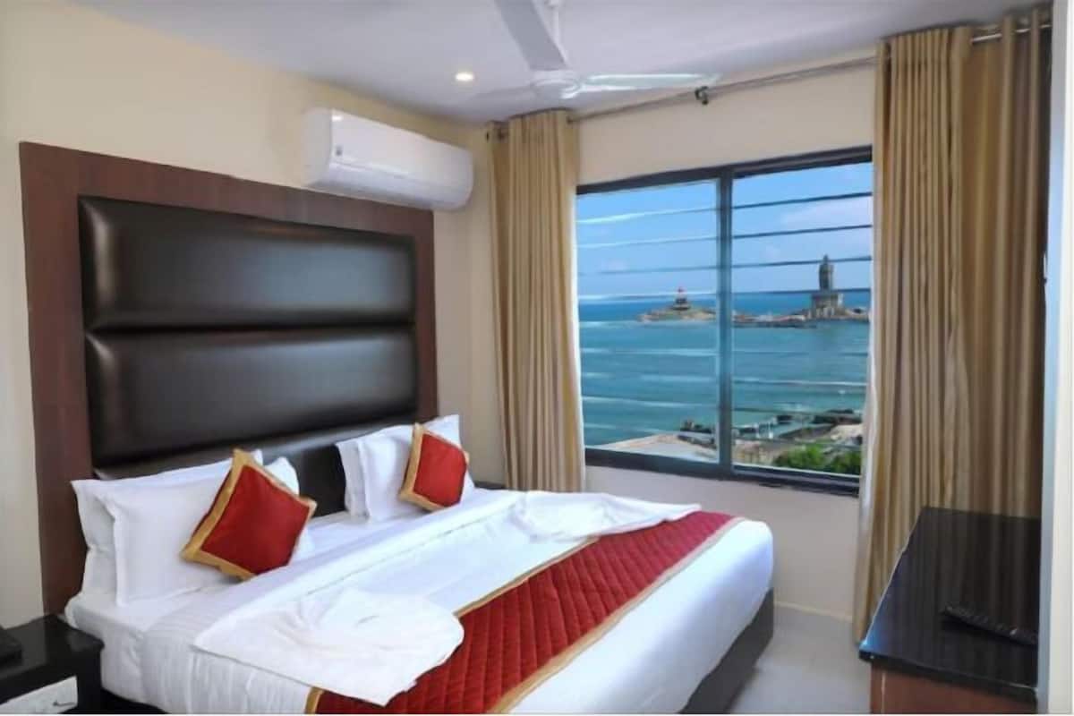 Ein Hotelzimmer mit einem großen Bett, einem Kopfteil, einem Fernseher und einem Fenster mit Blick auf das Meer und eine ferne Insel.