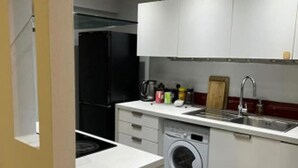 A compact kitchen with white cabinets, a built-in washing machine, and a black refrigerator.