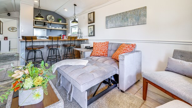 Un salon moderne avec un canapé gris, des coussins à motifs orange et un arrangement floral en guise de décoration centrale.