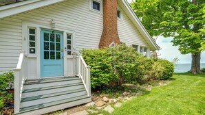 A white house with a blue door, a brick chimney, and a stone pathway leading to the front steps.