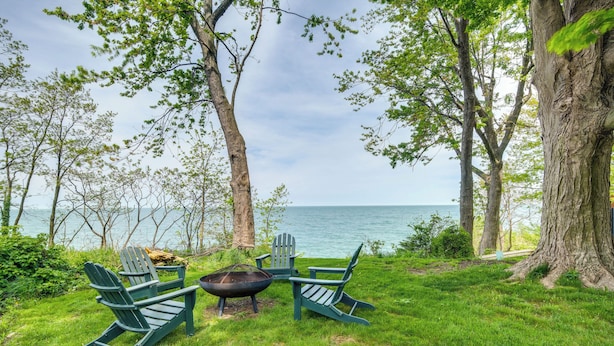A grassy area with two Adirondack chairs and a fire pit, overlooking a body of water.