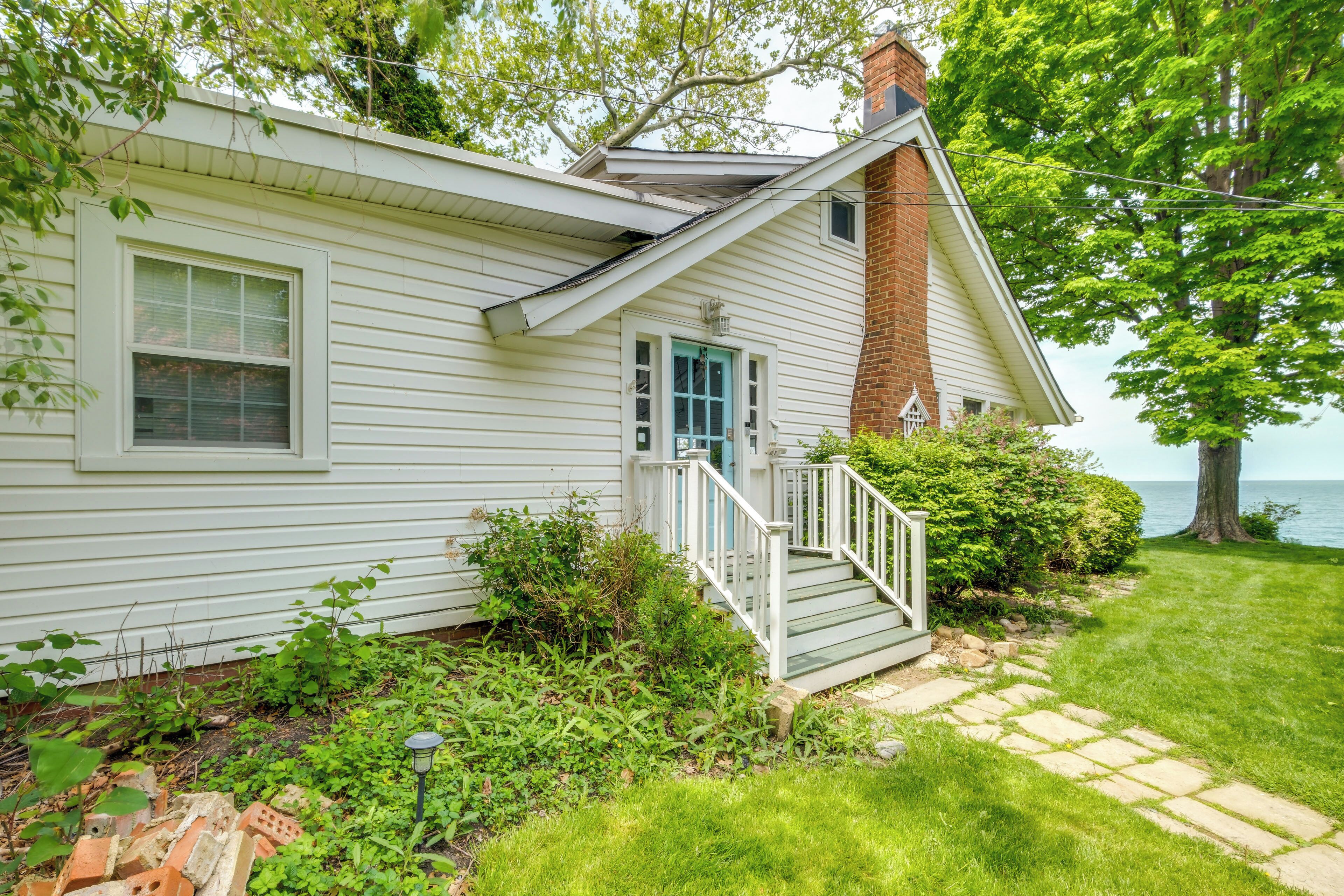 A white house with a brick chimney, a front porch, and a view of the water.