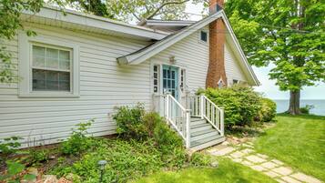 A white house with a brick chimney, a front porch, and a view of the water.
