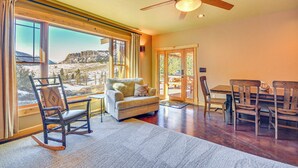 A cozy living room with a sofa, chairs, and a dining table. A large window offers a view of a snowy landscape. - Remote Mountainside Cabin By Stillwater River (Nye)