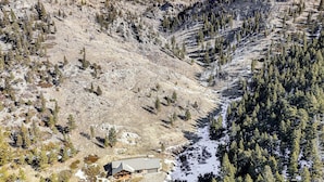 A lodge with a metal roof and stone walls, surrounded by a mountainous landscape with sparse trees and snow patches. - Remote Mountainside Cabin By Stillwater River (Nye)