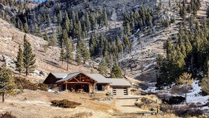 A log cabin with a metal roof, surrounded by a mountainous landscape and sparse trees. - Remote Mountainside Cabin By Stillwater River (Nye)
