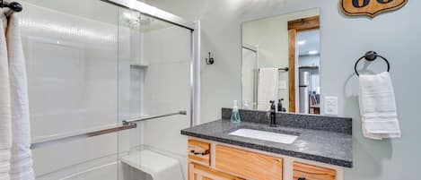 Un baño con cabina de ducha de vidrio, lavamanos con encimera de granito, armarios de madera y un espejo con un cartel de 'Route 66'.