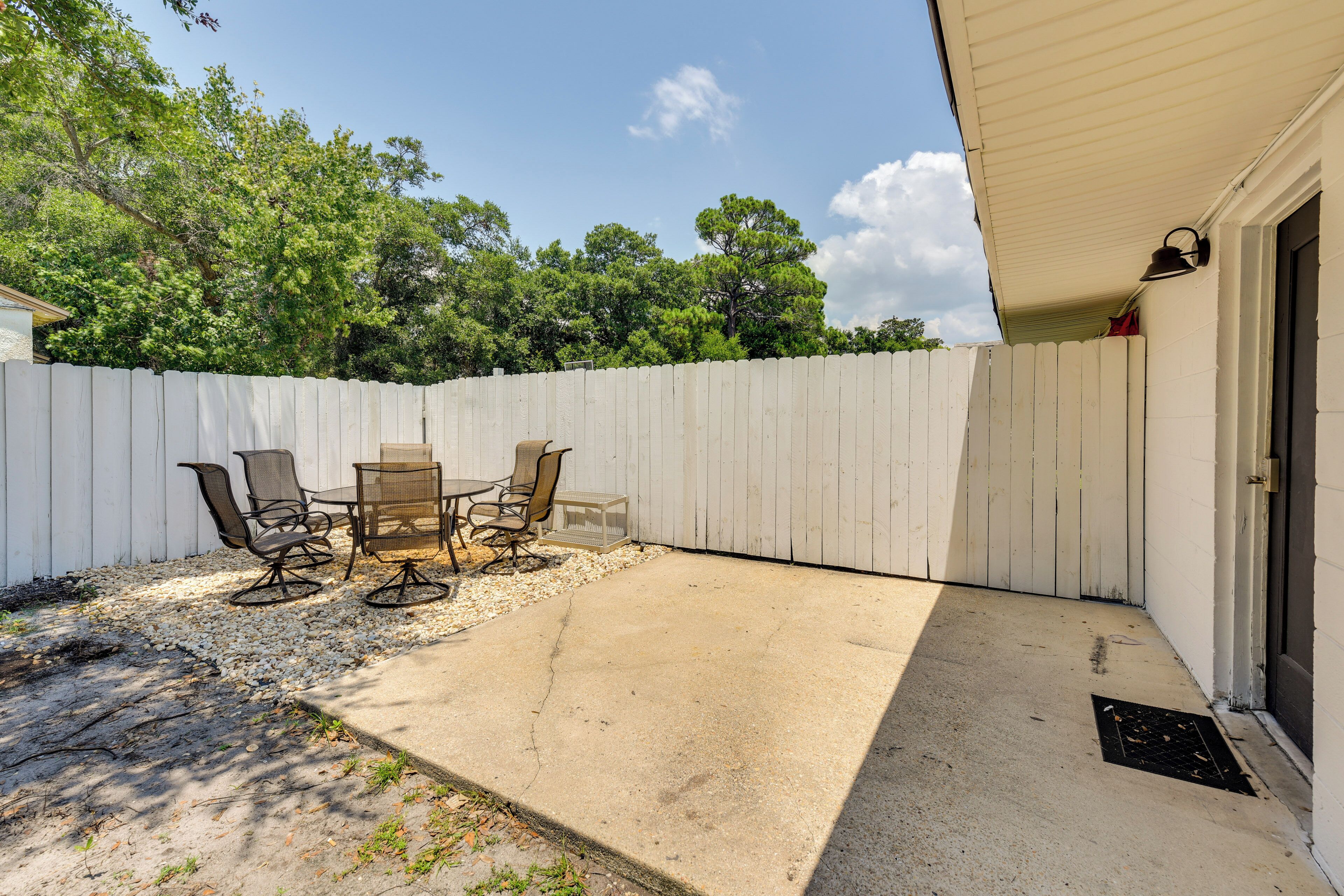 A patio area with a white fence, outdoor furniture, and a door to the right.