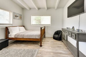 Quarto com cama de madeira, escrivaninha com gavetas, televisão e janela com persianas.