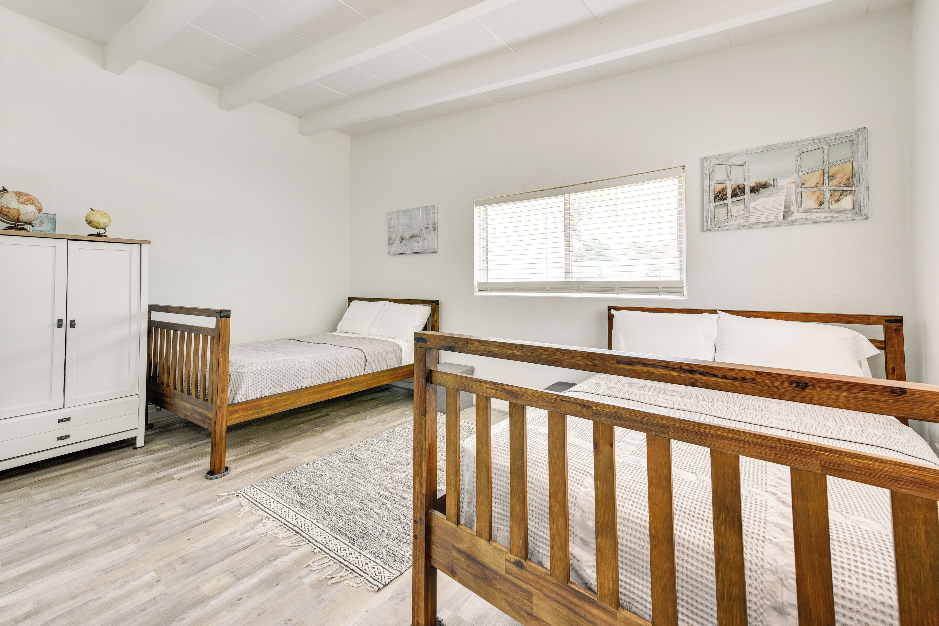 A bedroom with two wooden beds, a white wardrobe, and a window with blinds.