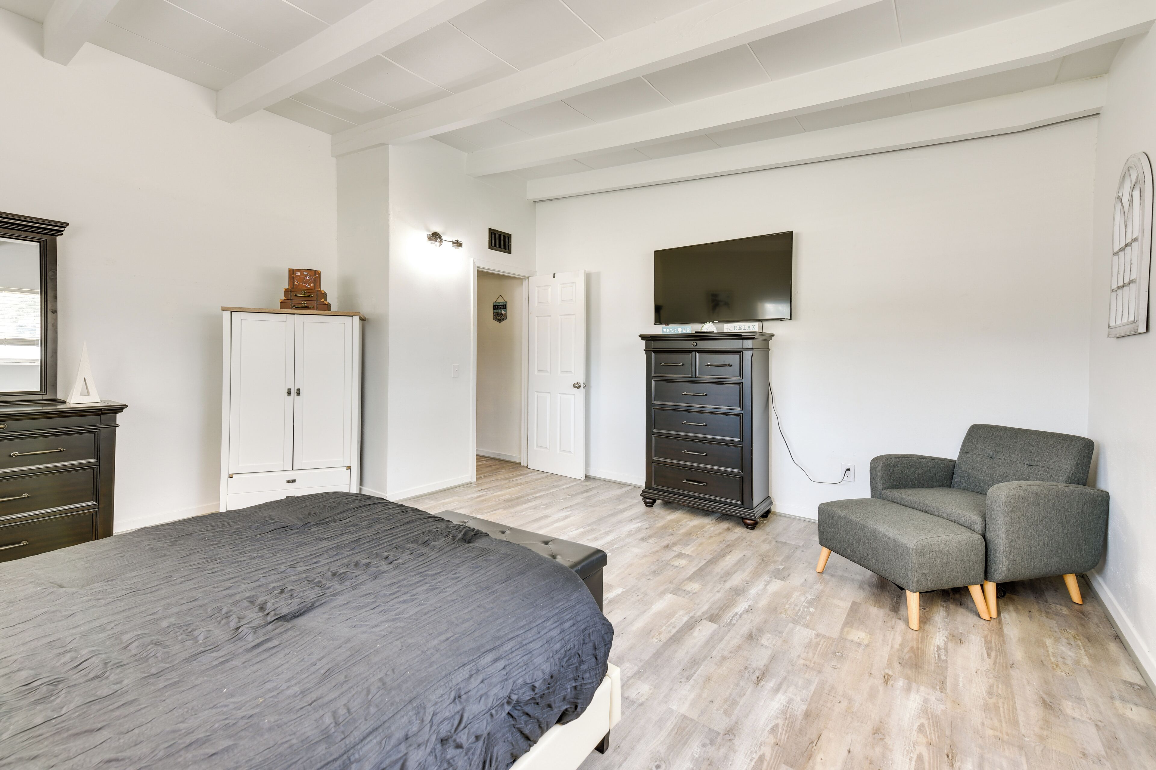 Een slaapkamer met een bed, een dressoir, een stoel en een televisie aan de muur.