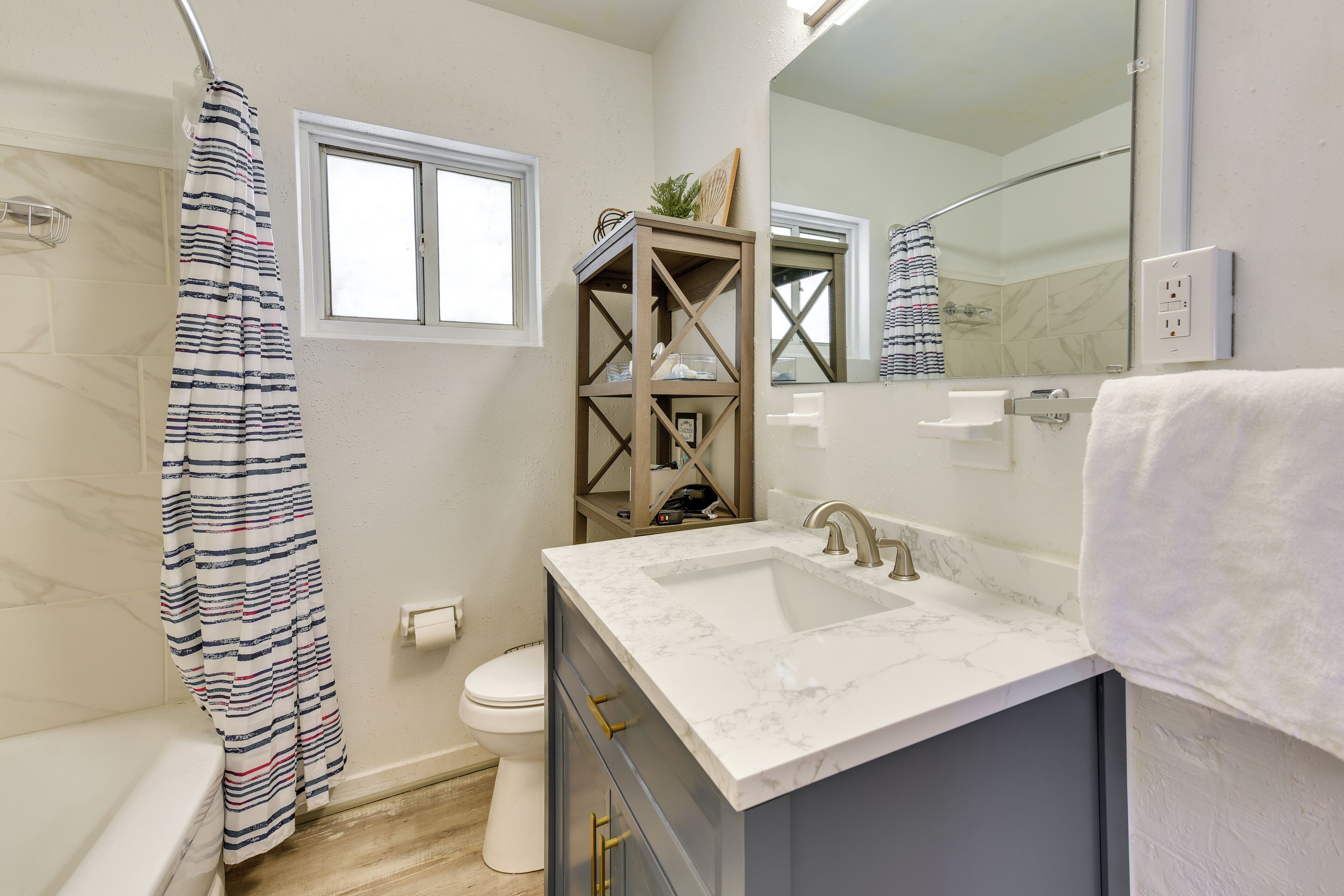 Un bagno con un WC bianco, una doccia con tenda a righe, un lavabo in marmo e uno scaffale in legno con uno specchio sopra.