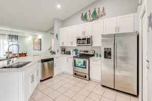 A modern kitchen with white cabinets, stainless steel appliances, and a tiled floor.
