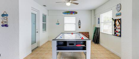 A room with a foosball table, a ceiling fan, and a window with blinds.