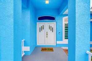 A blue building facade with a white door, a welcome mat, and a small window.