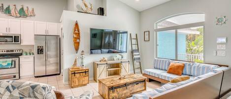 A modern living room with a sofa, coffee table, and TV. There is a kitchen with appliances and a dining area.