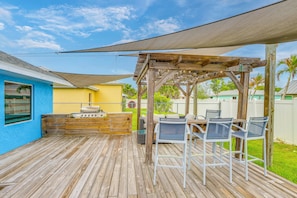 Eine Holzterrasse mit Grillplatz, Sitzgelegenheiten im Freien und einer Pergola, die Schatten spendet.