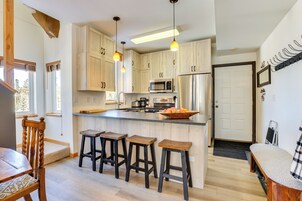 Una cocina moderna con armarios de madera, una isla central con taburetes, un refrigerador y un microondas.