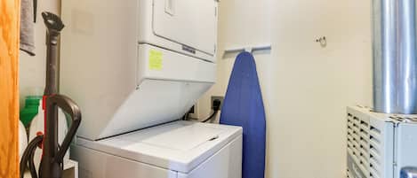 A laundry area with a front-loading washer and dryer, a blue ironing board, and a vacuum cleaner.