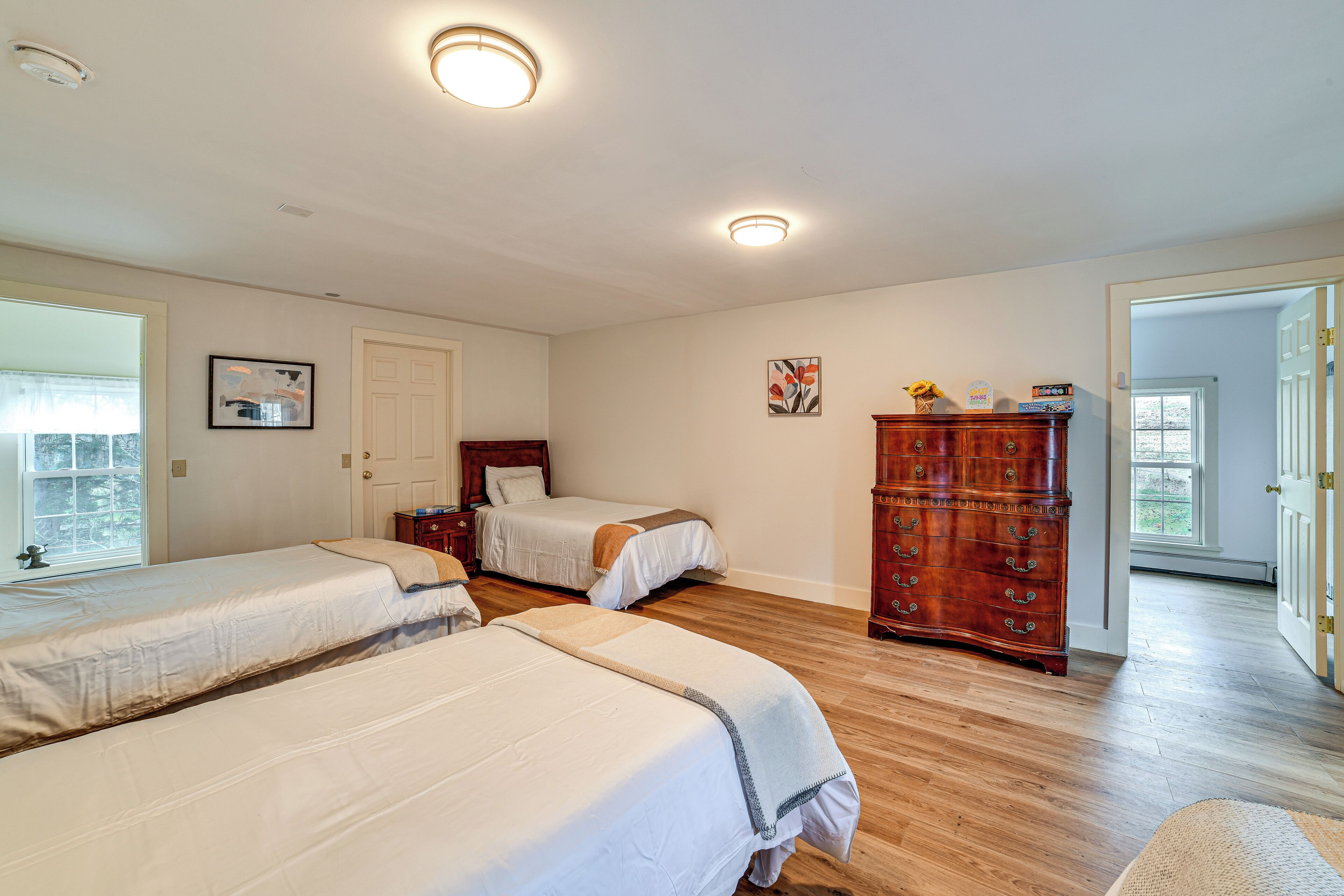 A room with three beds, a wooden dresser, and a door leading to another room.